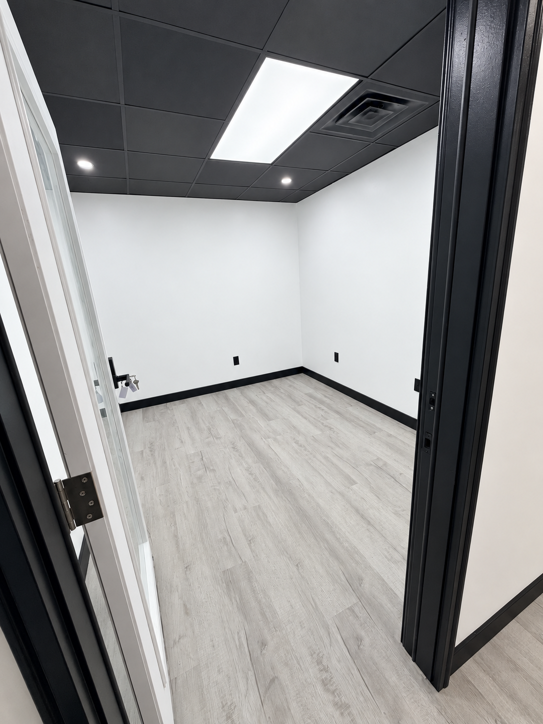 Private suite at Haus of Suites viewed through its doorway, with white walls, light wood-look flooring, and a black ceiling